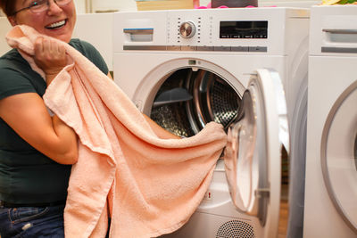 Midsection of happy woman holding towel by washing machine 