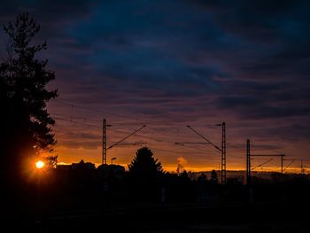 Silhouette trees and electricity pylon against dramatic sky during sunset