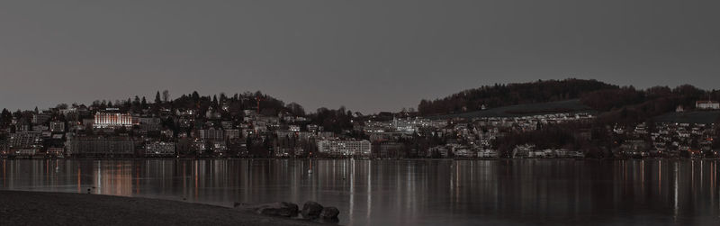 Illuminated city by river against clear sky at dusk