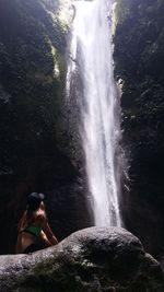 Midsection of woman on rock at waterfall