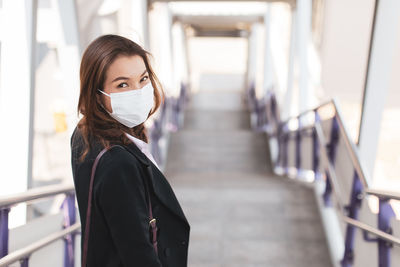Portrait of businesswoman wearing mask standing on staircase outdoors