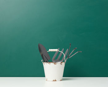 Miniature garden tools in a metal bucket on a green background, copy space