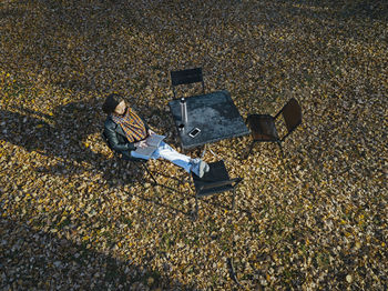 Drone view of woman reading book while sitting on chair at park during autumn season