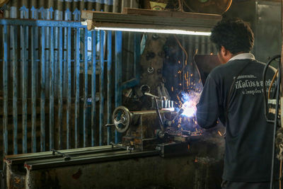 Rear view of man working at illuminated shop