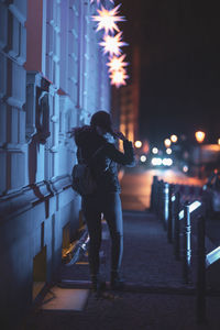 Full length of woman standing on sidewalk in illuminated city at night