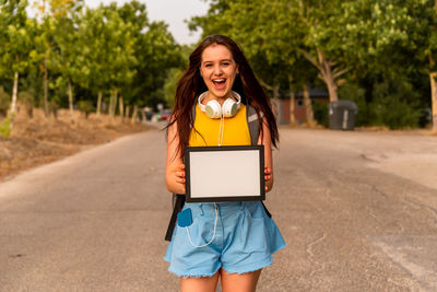 Portrait of smiling woman holding digital tablet while standing on road