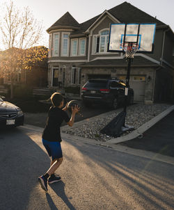 Full length of boy playing basketball on road by house