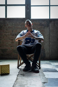Full length portrait of man sitting on chair against wall