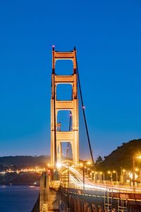 Low angle view of illuminated bridge against clear blue sky