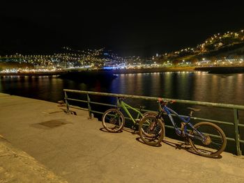 Bicycle by river against illuminated city at night