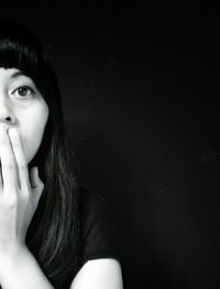 Portrait of young woman with hands covering mouth against black background