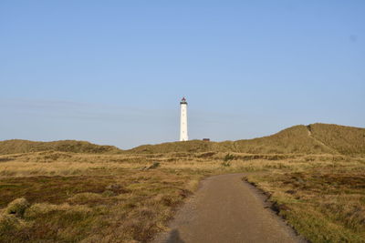 Lighthouse by road amidst buildings against clear sky