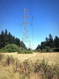 Low angle view of electricity pylon on field against clear sky