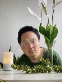 Portrait of young asian man with aromatherapy diffuser, peace lilies, branches on white background 