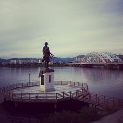 Statue of man standing by bridge against sky