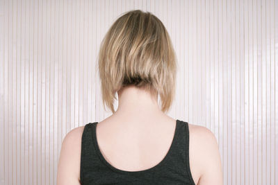 Rear view of young woman with short hair against wall