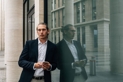 Businessman using smart phone while standing by window