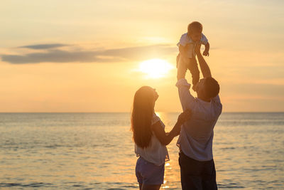 Full length of couple standing on beach during sunset