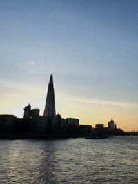 Sea by buildings against sky during sunset