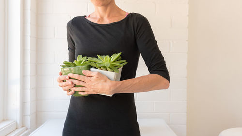 Midsection of woman holding plant against wall