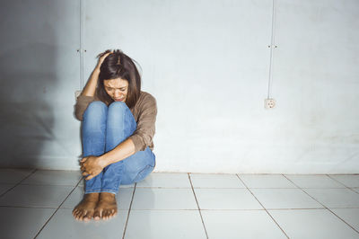 Young woman sitting on floor against wall