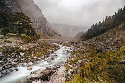 Scenic view of stream amidst mountains against sky