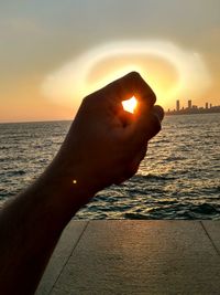 Close-up of hand against sea during sunset