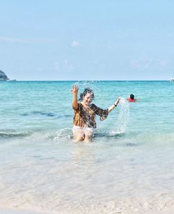 Woman splashing water on shore at beach against sky