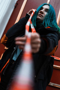 Low angle view of young woman with dyed hair holding ribbon while standing at home