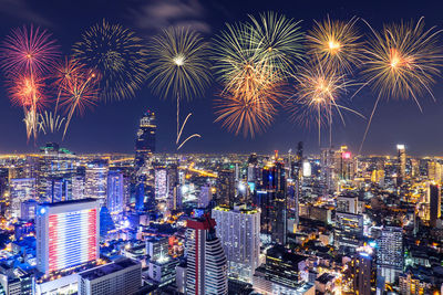 Firework display in city against sky at night