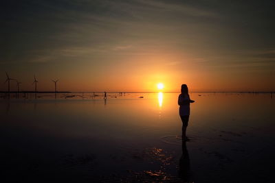 Silhouette of people fishing in sea at sunset