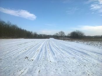 Tire tracks on snowy landscape against sky