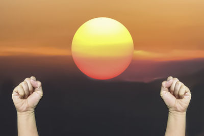 Close-up of hand holding sun during sunset