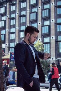 Side view of businessman checking time while standing in city