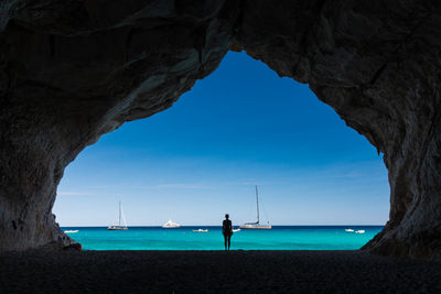 Silhouette woman standing in cave at beach against sea and sky