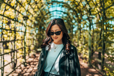 Young woman wearing sunglasses standing against plants