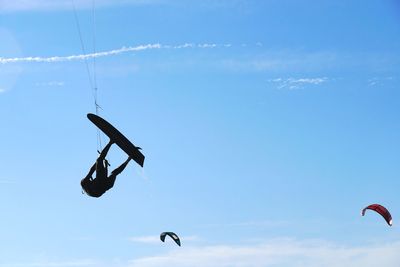 Low angle view of silhouette person kiteboarding against blue sky