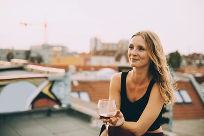 Thoughtful smiling woman having wine while sitting on terrace during rooftop party