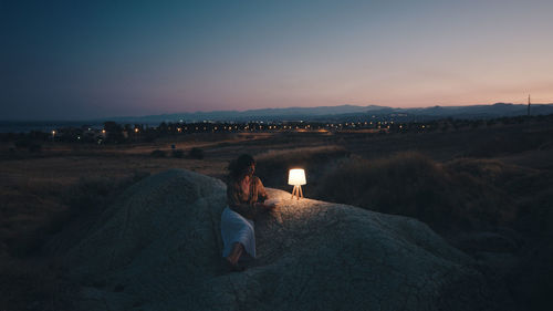 Woman reads a book in the evening on a rock with lamp