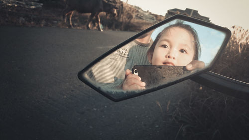 Portrait of boy holding camera while standing on mirror