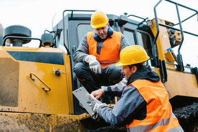 People working on construction vehicle against sky