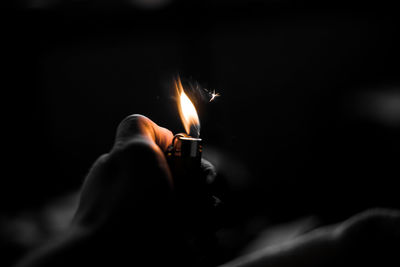 Close-up of hand holding lit candle against black background