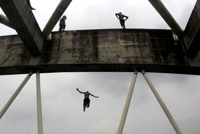 Low angle view of men jumping from bridge against sky