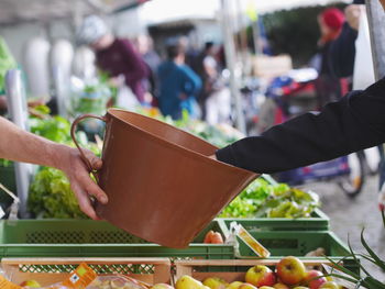 Cropped hand on vendor giving bucket with costumer in vegetable market