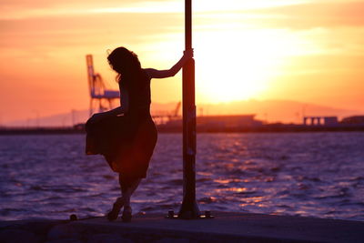 Silhouette woman standing on pier over sea against sky during sunset