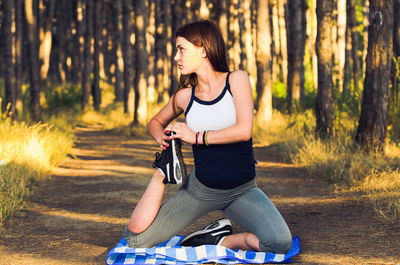 Young woman stretching body on exercise mat against trees in forest during sunset