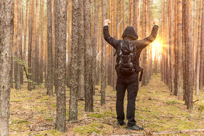 Man in hooded shirt clenching fists against trees