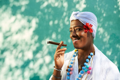 Portrait of smiling woman smoking cigar against wall