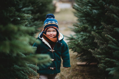 Adorable child wearing wool coat walking between christmas trees