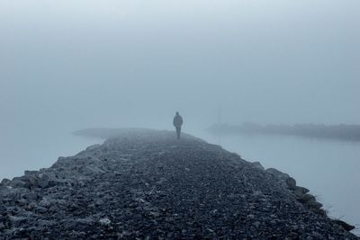 Mid distant view of man walking on groyne amidst sea during foggy weather